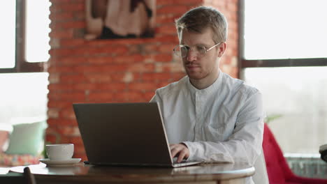 Ein-Erwachsener-Mann-In-Weißem-Hemd-Und-Brille-Sendet-Eine-Nachricht-Im-Online-Chat-Mit-Einem-Modernen-Laptop,-Der-Im-Café-Arbeitet